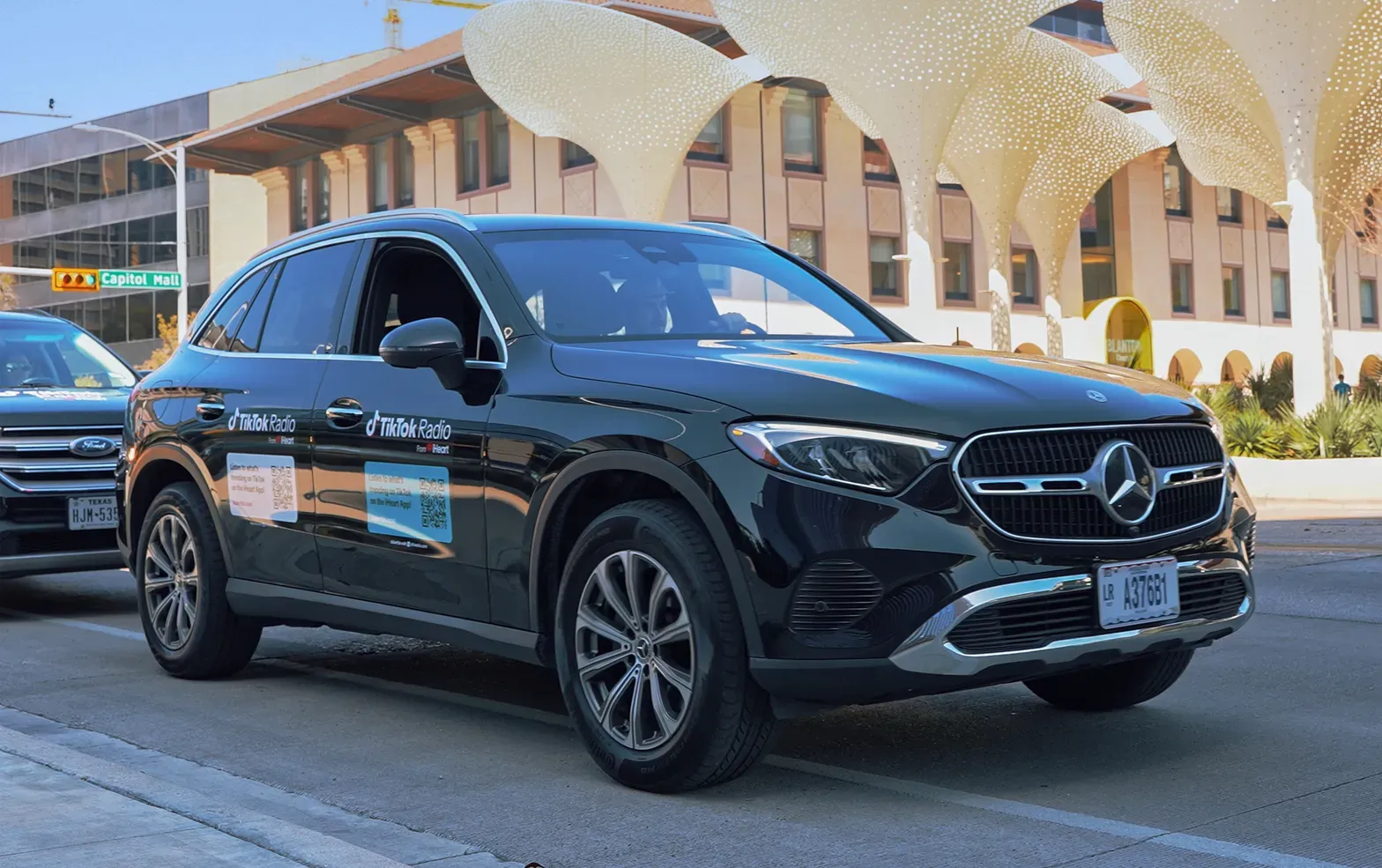 Black Mercedes SUV with TikTok Radio door and panel stickers parked on a busy downtown street