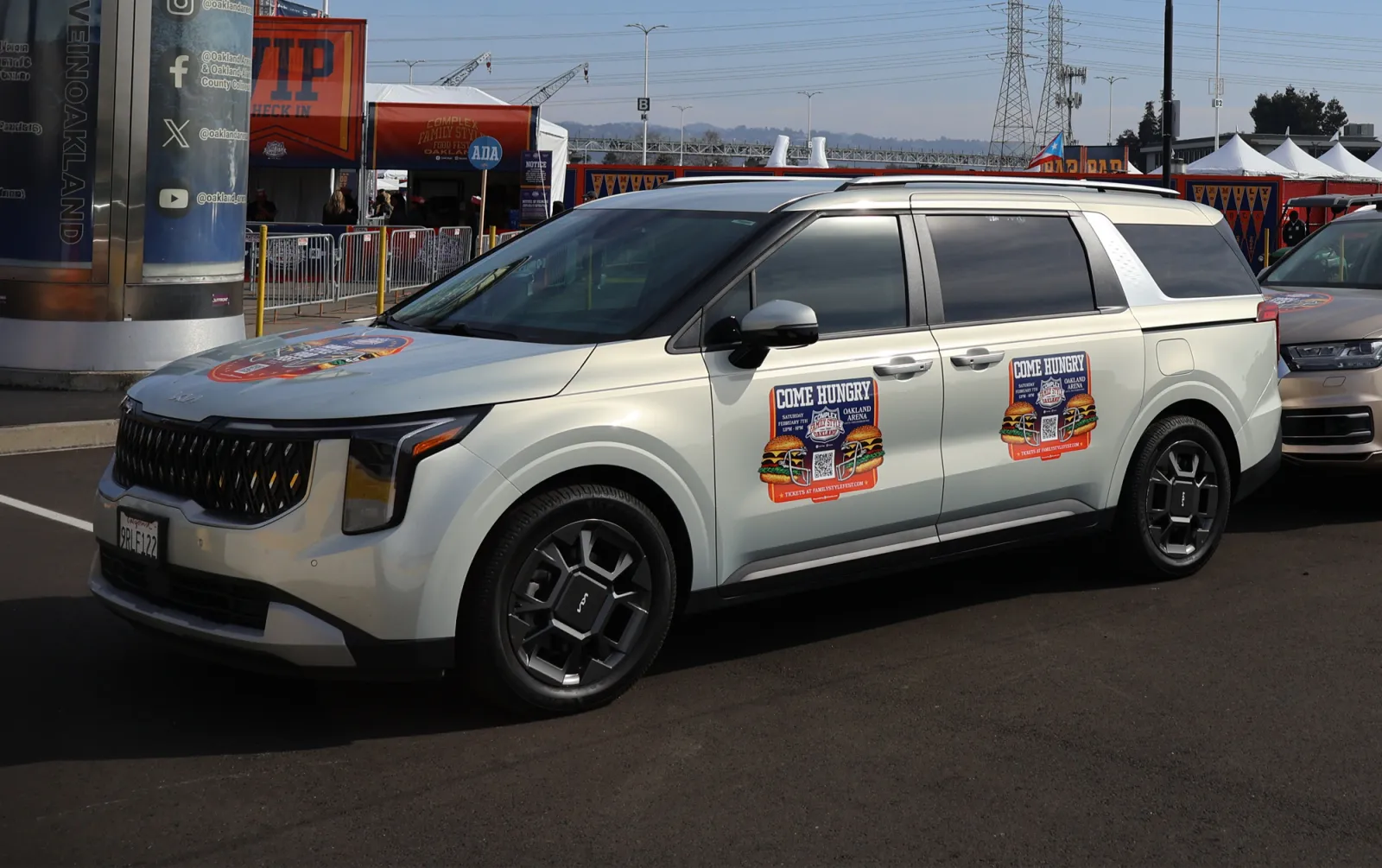 Silver Kia van with a Complex Come Hungry event campaign at an arena